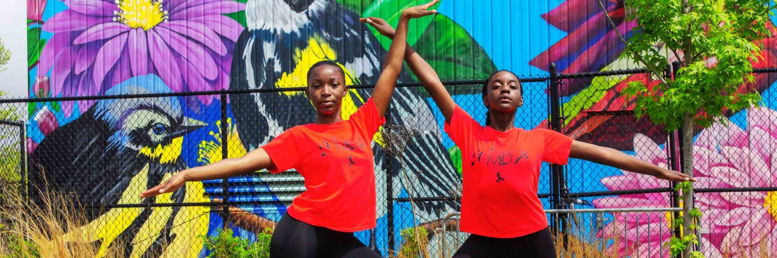 girls in red shirts in front of mural